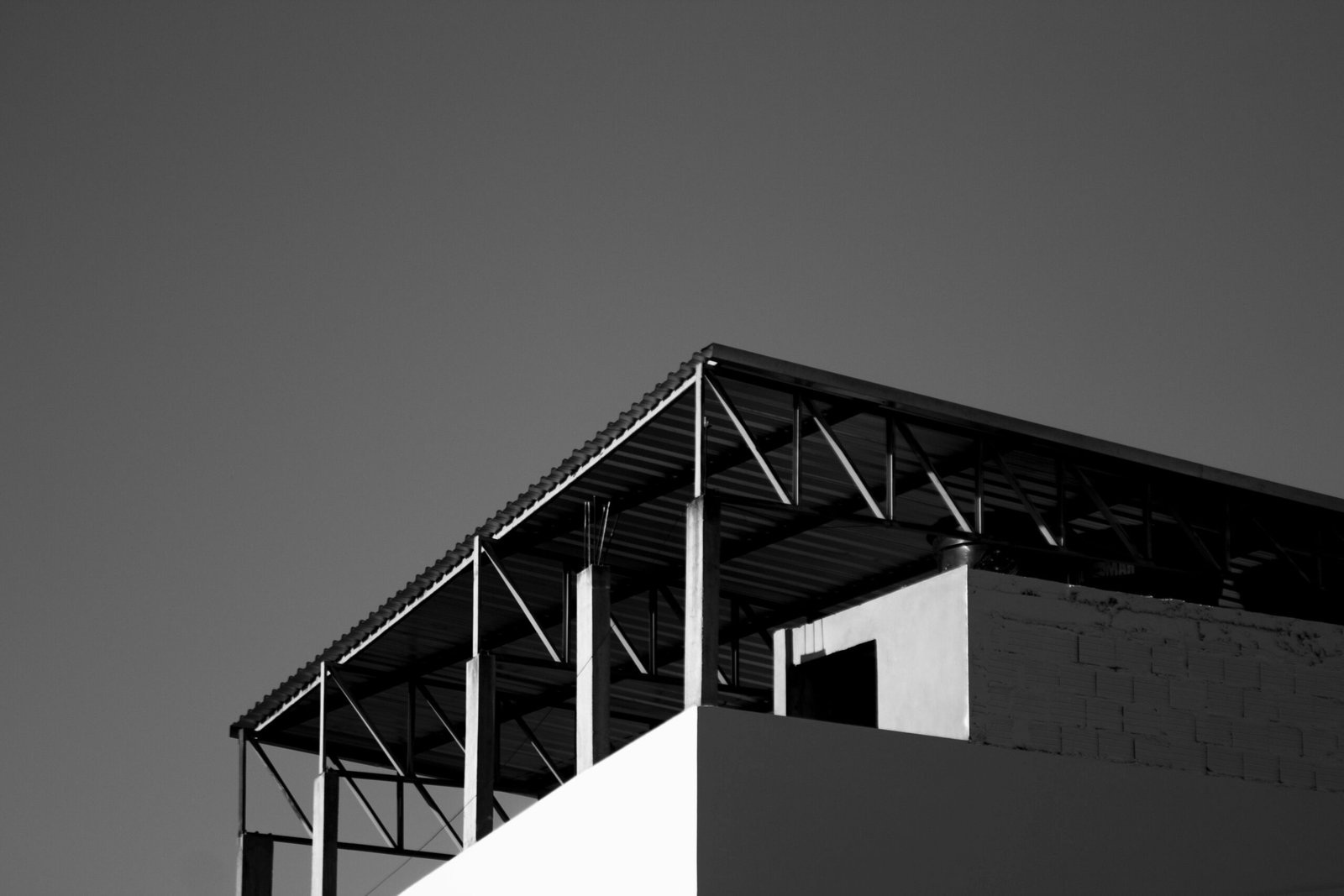 Black and white photo of a sunlit modern building with a clear sky and metal beams.